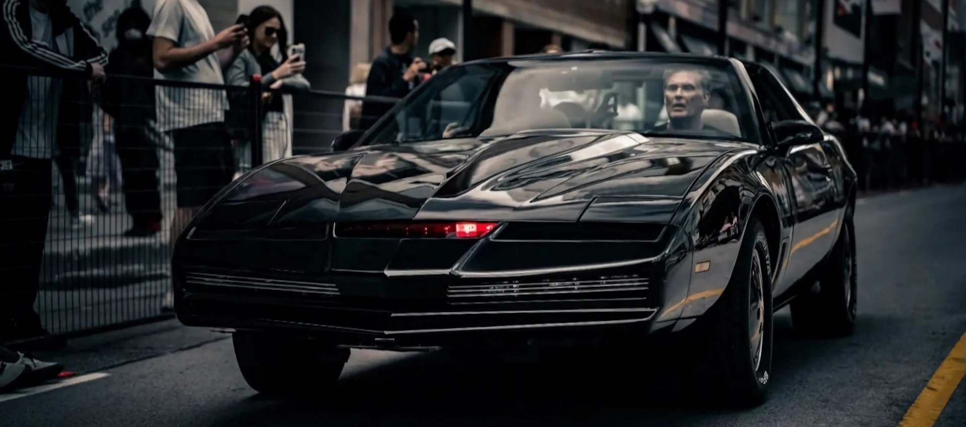 David Hasselhoff sitting in the driver's seat and driving the authentic Knight Rider KITT replica car on a city street in Toronto.